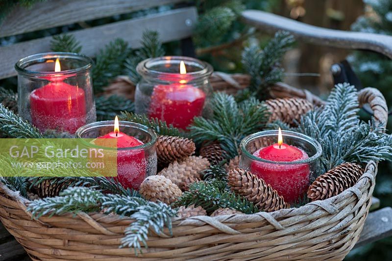 A snowy bench decorated with a fir garland and baskets with greenery and candles