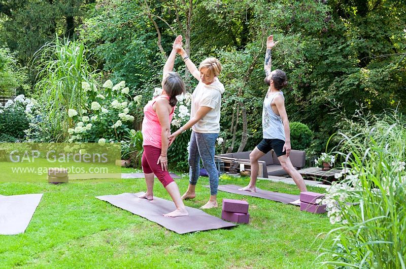 Yoga course in a green garden. The teacher is correcting the position called Virabhadrasana