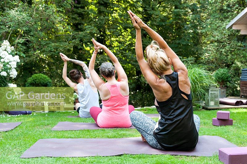 Yoga in a green garden. 3 people are in the position called lateral flexion.