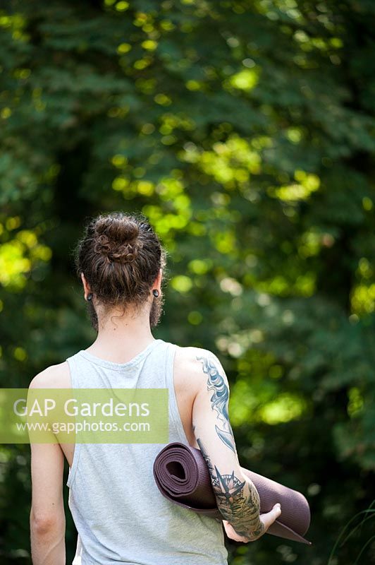 A person holding a yoga mat in the garden