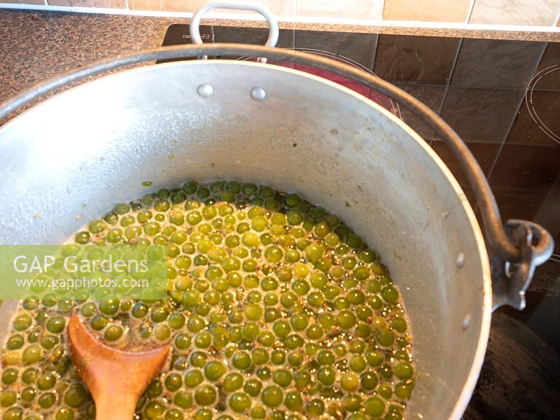 Stirring boiling grape mixture in metal pan to make jam.