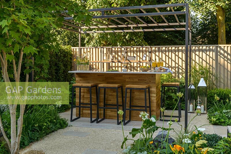 Bespoke pergola over wooden outdoor bar with stools on terrace. 'Landform Garden Bar', RHS Hampton Flower Show, 2018