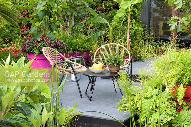 Seating on graphite porcelain paving. 'B and Q Bursting Busy Lizzie Garden', RHS hampton Flower Show, 2018