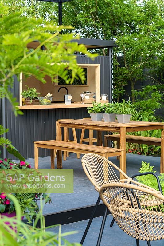 Highline metal shed, Table and benches on graphite porcelain paving. 'B and Q Bursting Busy Lizzie Garden' RHS Hampton Flower Show, 2018 