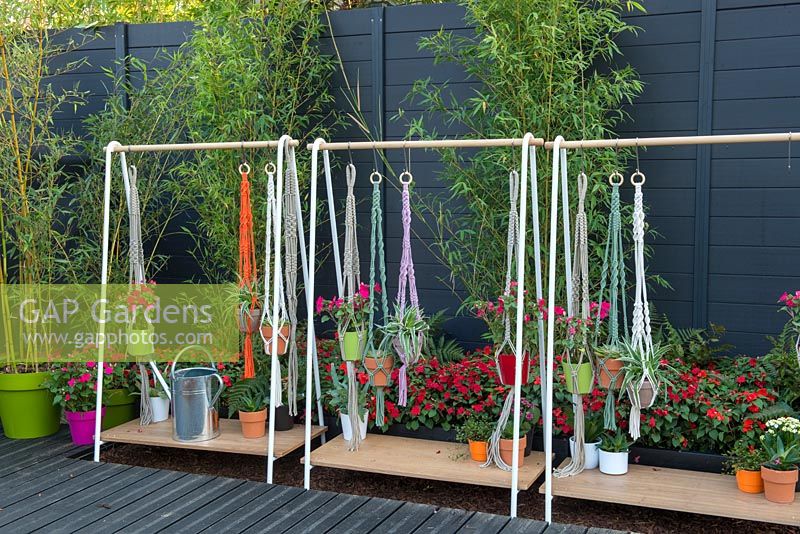 Potted plants hanging on stands by macrame pot holders. BandQ Bursting Busy Lizzie Garden, Sponsored by BandQ, RHS Hampton Court Flower Show, 2018.