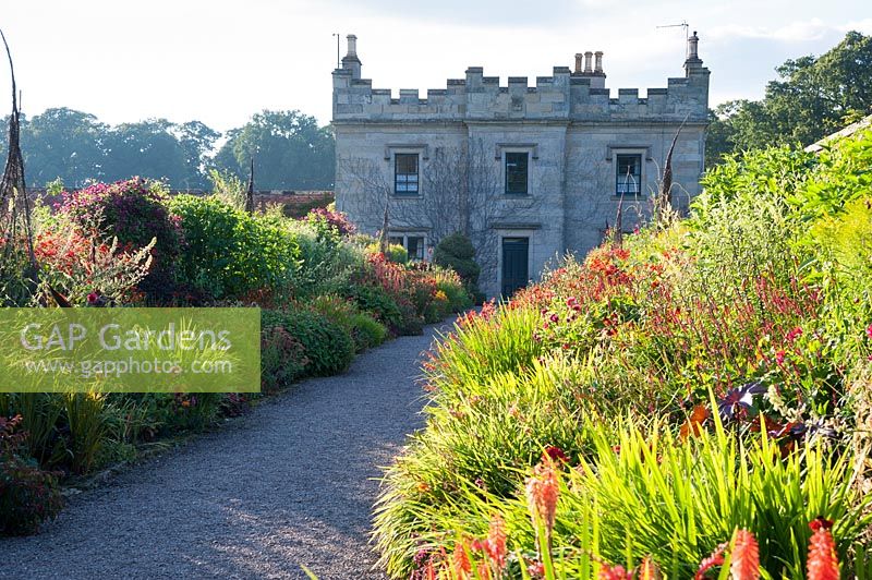 View past hot-coloured borders to castle. Floors Castle, Kelso, Roxburghshire, Scotland, UK.
