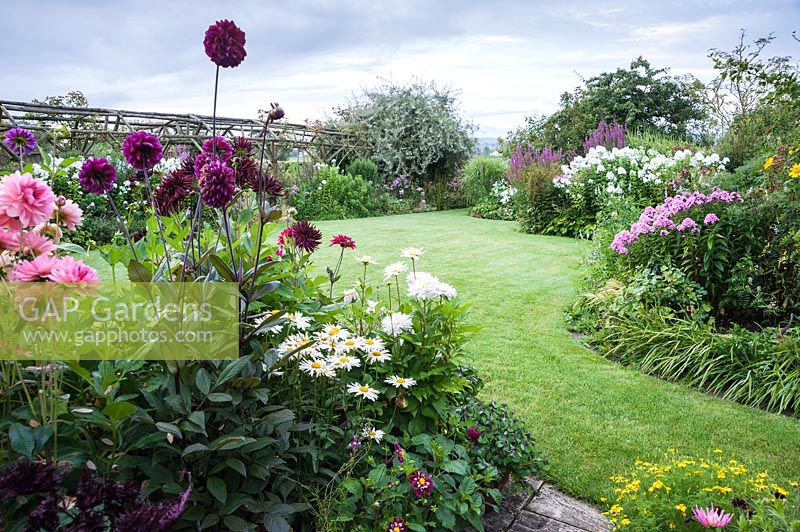 View of curved, flowering borders surrounding mown lawn. Hilltop, Stour Provost, Dorset, UK. 