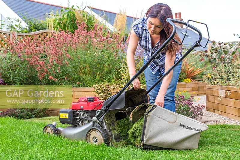 Woman emptying grass collector on petrol mower. 