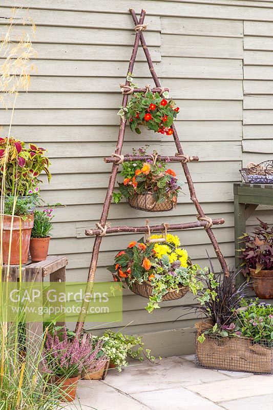 Wire baskets lined and planted with colourful bedding plant tied with rope to vertical hazel stick planter. 