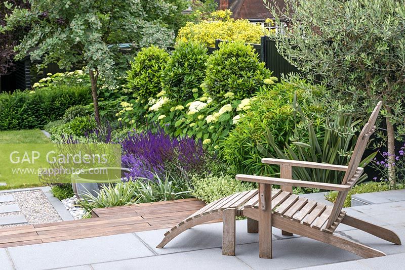 Adirondack chair on terrace with border of phormium, euphorbia, Hydrangea and Salvia