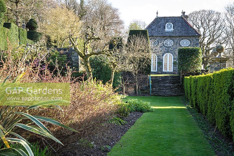 A grassy path between a box hedge and a mixed border leads towards the Orangery at Plas Brondanw, Penrhyndeudraeth, Gwynedd, Wales