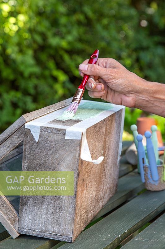 Woman painting area of wooden box marked with masking tape. 