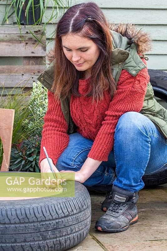 Woman marking where to make holes in base of planter to attach to tyre.