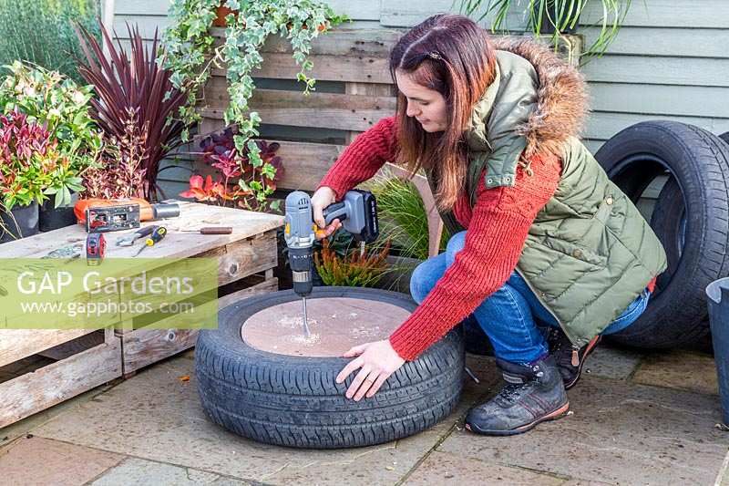 Woman using a drill to create drainage holes in base of tyre planter.