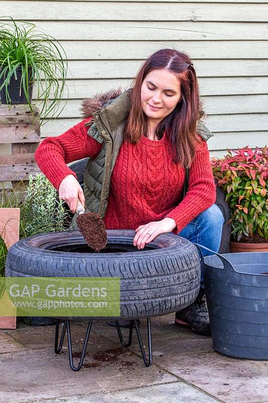Woman adding compost into tyre container.