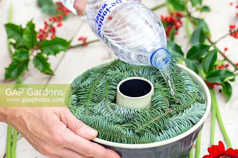 Woman pouring de-ironised water into bundt cake tin full of cut plant material to create frozen floral arrangement.