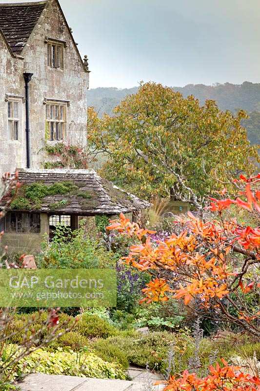 View of house through dramatic autumn shrubs and trees. Gravetye Manor, Sussex, UK. 