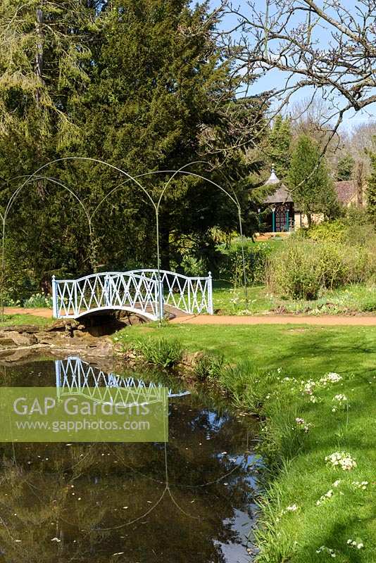 Blue metal arched bridge over pond with arch supports, trees and Indian kiosk in distance
