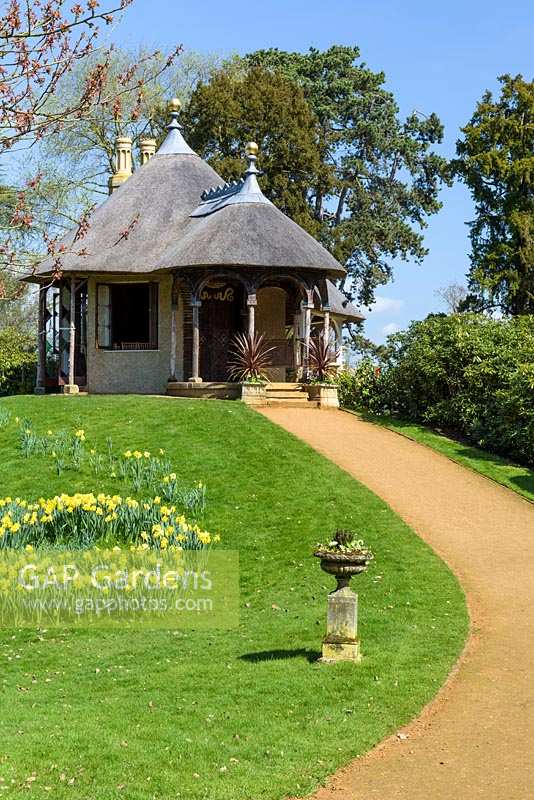 Curved path leading to the Swiss-style thatched cottage, next to lawn with daffodils
