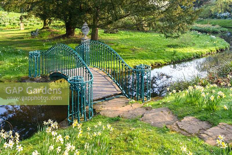 Arched foot-bridge with painted metal railing over stream with grassy banks
