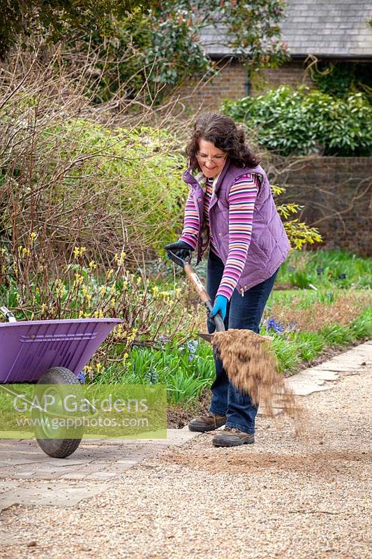 Woman replenishing gravel on paths. 