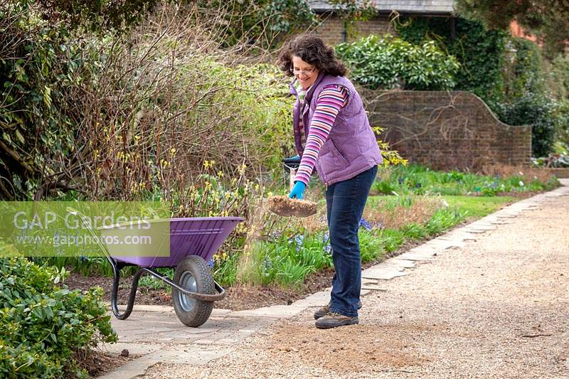 Woman replenishing gravel on paths.