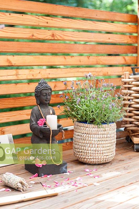 Decorated with Buddha holding a candle, sage to smudge and incense sticks on wooden balcony. 