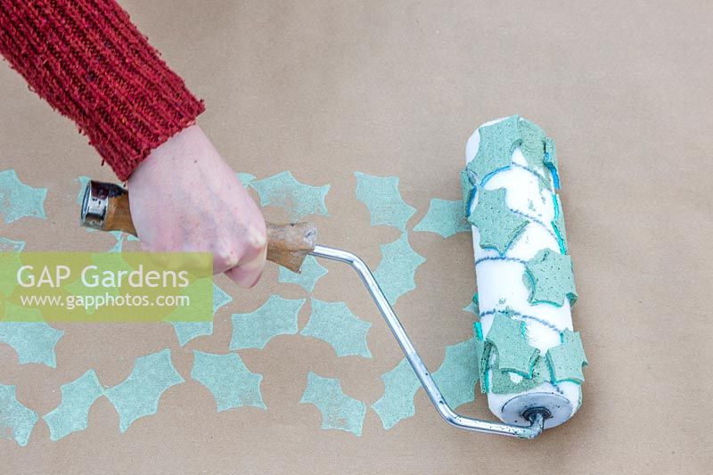 Using roller with foam patterns to create holly pattern on craft wrapping paper.