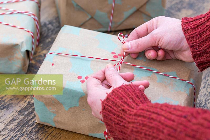 Woman tying bakers twine bow on present wrapped with handmade craft wrapping paper.
