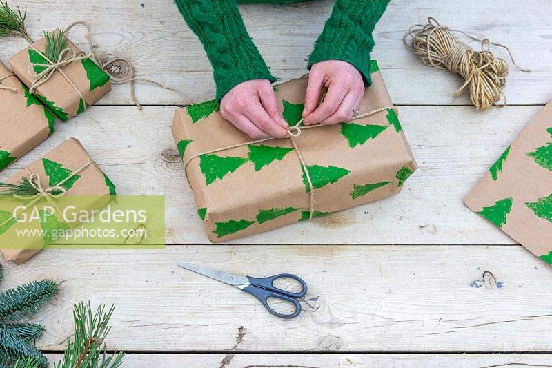 Woman tying string bow on christmas gift wrapped with hand printed wrapping paper.
