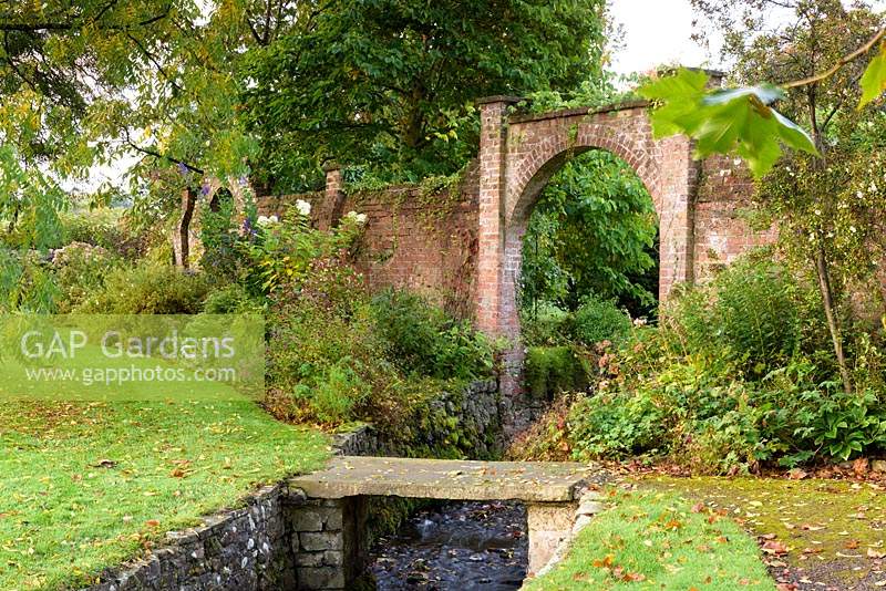 An archway in the walled Round Garden frames a stream at Llanover Gardens, Monmouthshire, UK. 