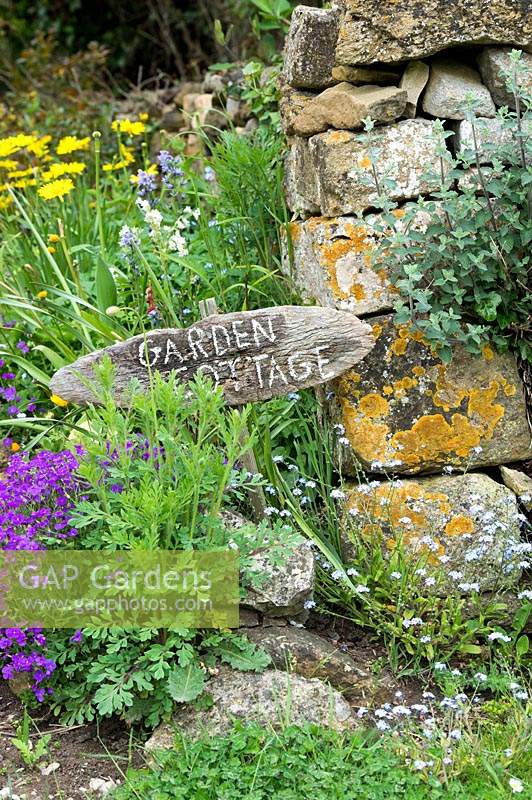 'Garden cottage' wooden sign for a house near stone wall

