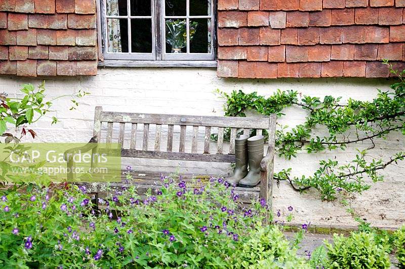 Wellies on old wooden bench outside cottage. Copyhold Hollow, Sussex, UK. 
