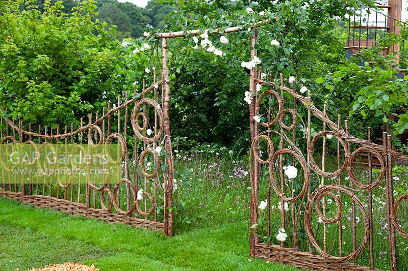 Hazel and willow decorative fence in pattern of circles either side of an arch, in the show garden 'Belmond Enchanted Gardens 