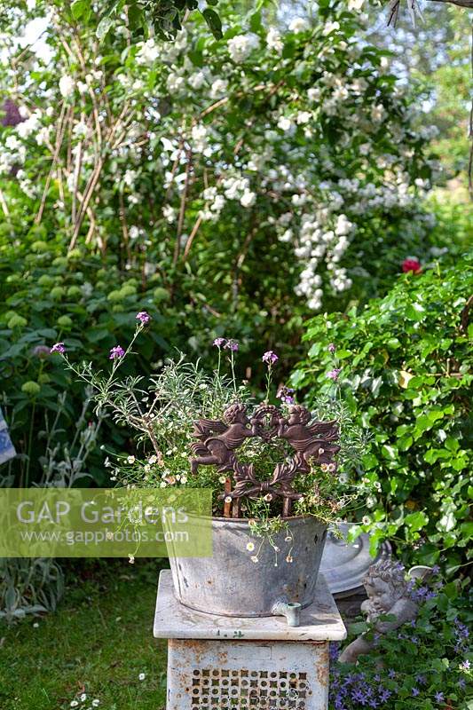 Vintage metal tub on a plinth, container with mixed planting and ornamental figures
