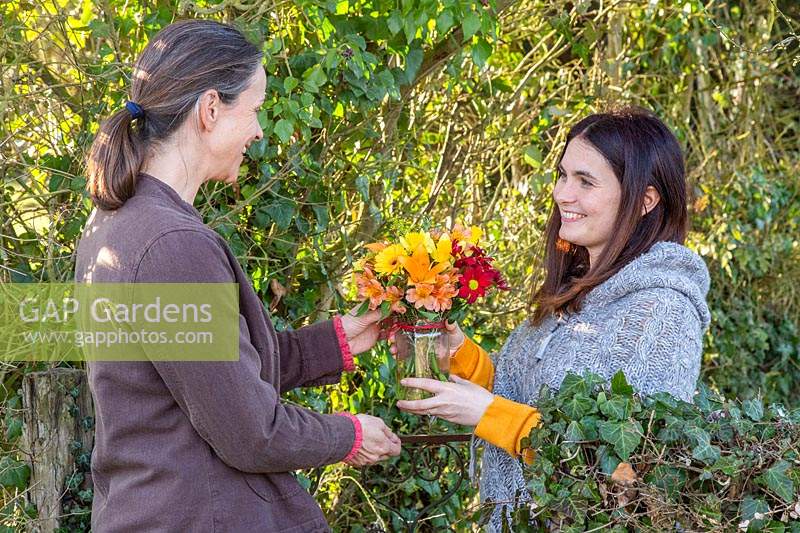 Two women exchanging a gift of a vase of flowers. 