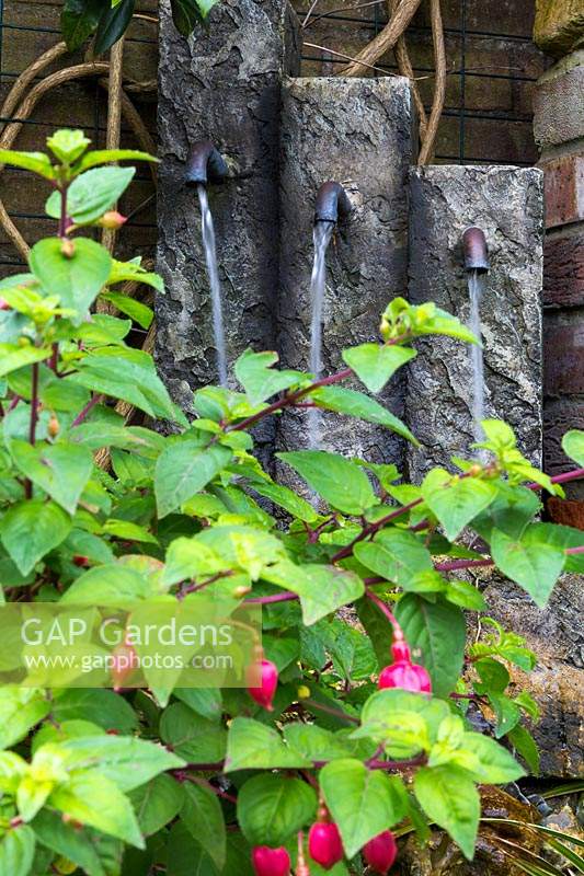 Water feature in a shady corner with a Fuchsia in front 