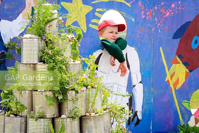 A pupil poses for the camera in school garden, with rocket pyramid made of ribbed silver tin cans growing various plants. RHS Malvern Spring Festival, 2017. O Beoley -wan-Kenobi, Beoley Primary School.