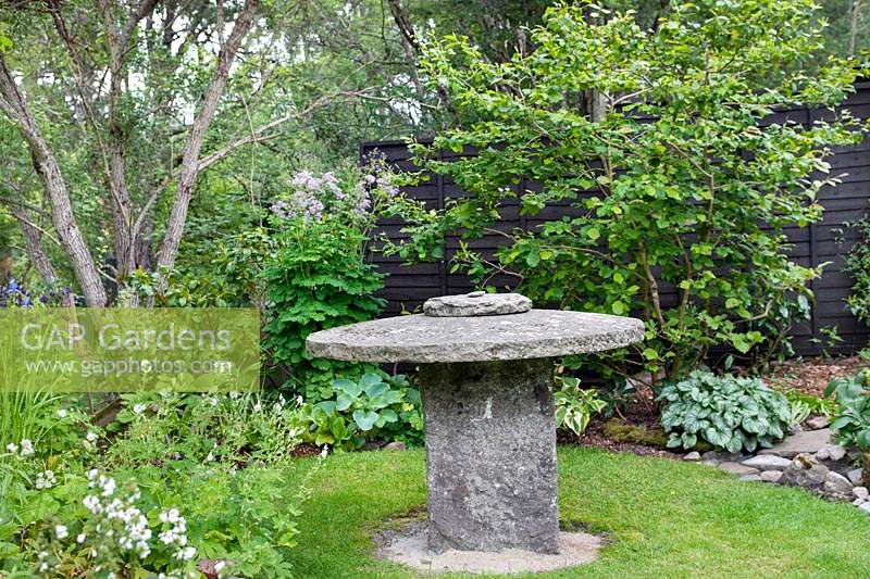 Old millstone used as a table, set in lawn surrounded by mixed beds

