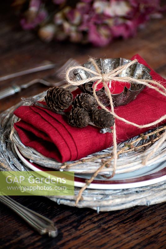 Place setting with wicker mats plus red linen napkin, cones and candle tied with string