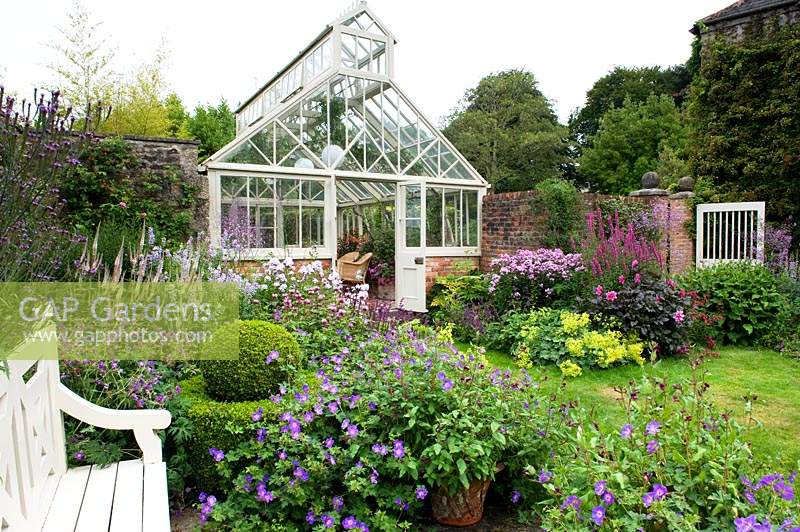 Traditional wood and brick glasshouse surrounded by flowering perennial borders in walled garden. Bosvigo House, Cornwall, UK.