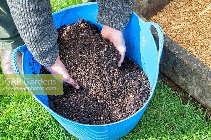 Gardener mixing alpine grit into compost in a trug.
