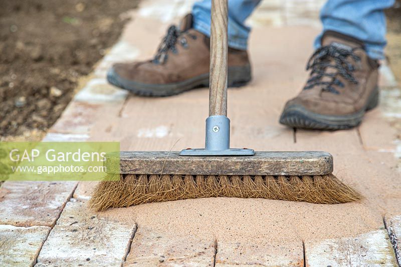 Man using broom to disperse kiln dried sand and fill gaps in newly laid pathway. 