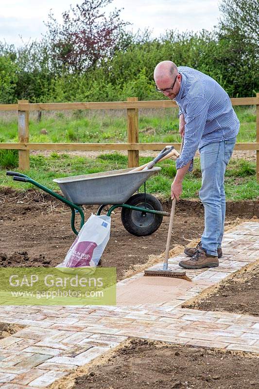 Man using broom to disperse kiln dried sand and fill gaps in newly laid paths. 