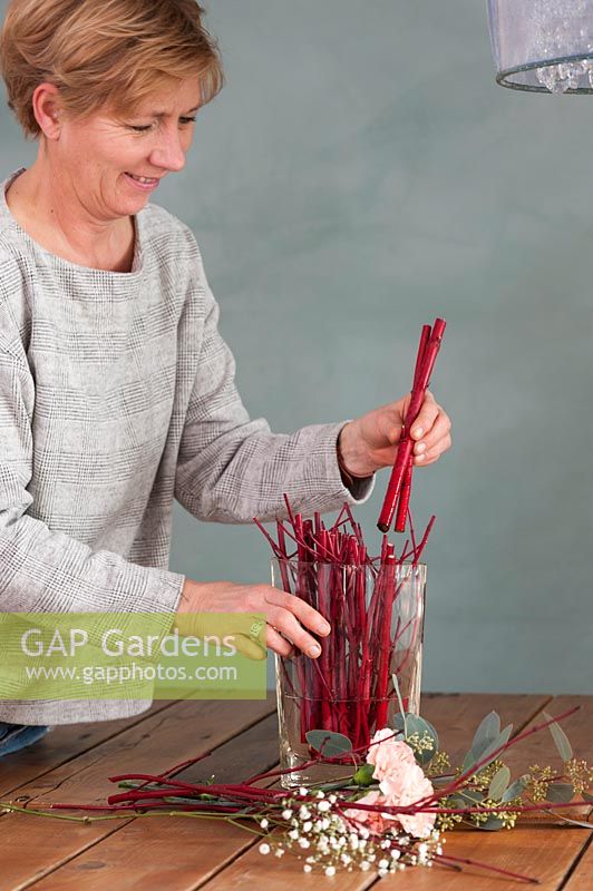Woman arranging stems of Cornus - Dogwood in vase to create modern floral arrangement. 

