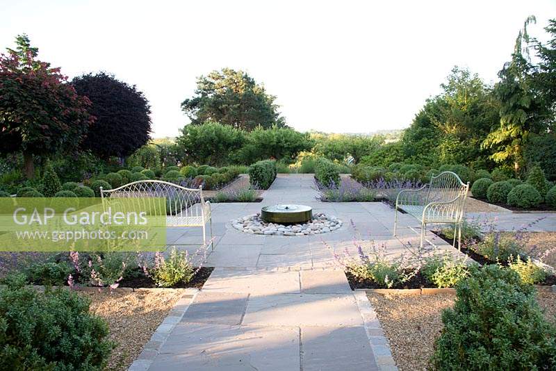 Formal garden with seating, central millstone water feature and topiary, overlooking countryside. 
