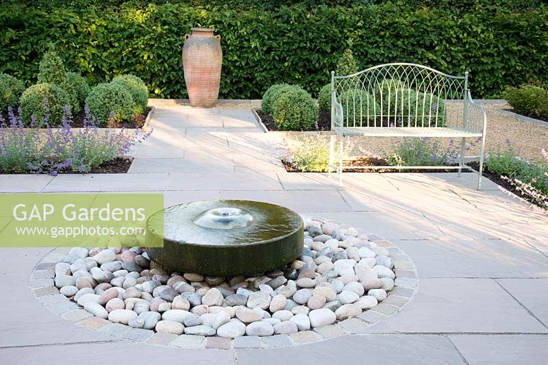 Formal garden with seating, central millstone water feature and topiary