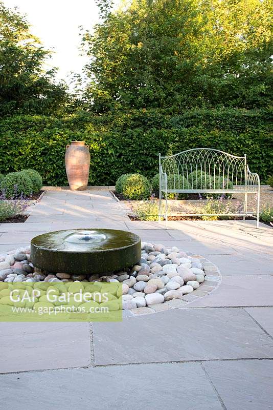 Formal garden with seating, circular millstone water feature and topiary