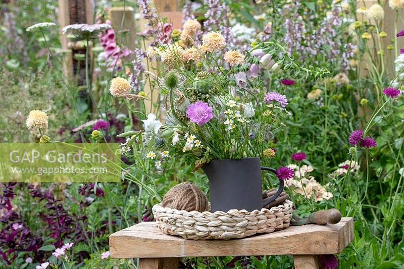 Cut flowers in a jug in front of an overgrown flower border in the BBC Springwatch garden at RHS Hampton Court Flower Show 2019 - Designed by Jo Thompson in consultation with wildlife gardener Kate Bradbury