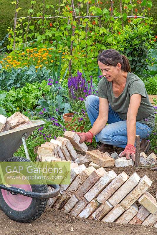 Woman adding second layer of brick to sawtooth raised bed